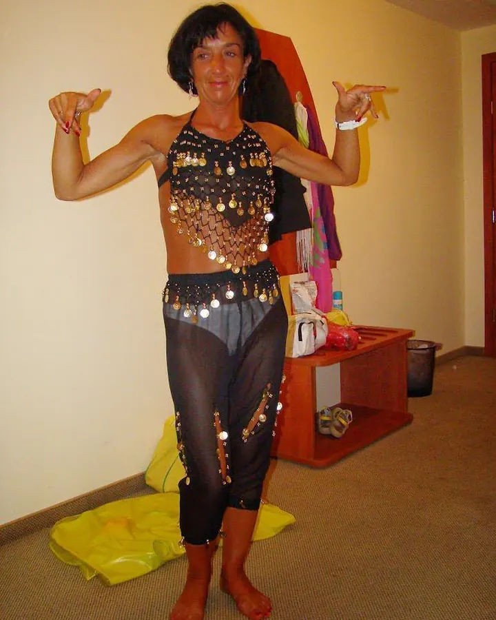 Femme en tenue de danse orientale, avec des franges métalliques, pointant vers elle-même.