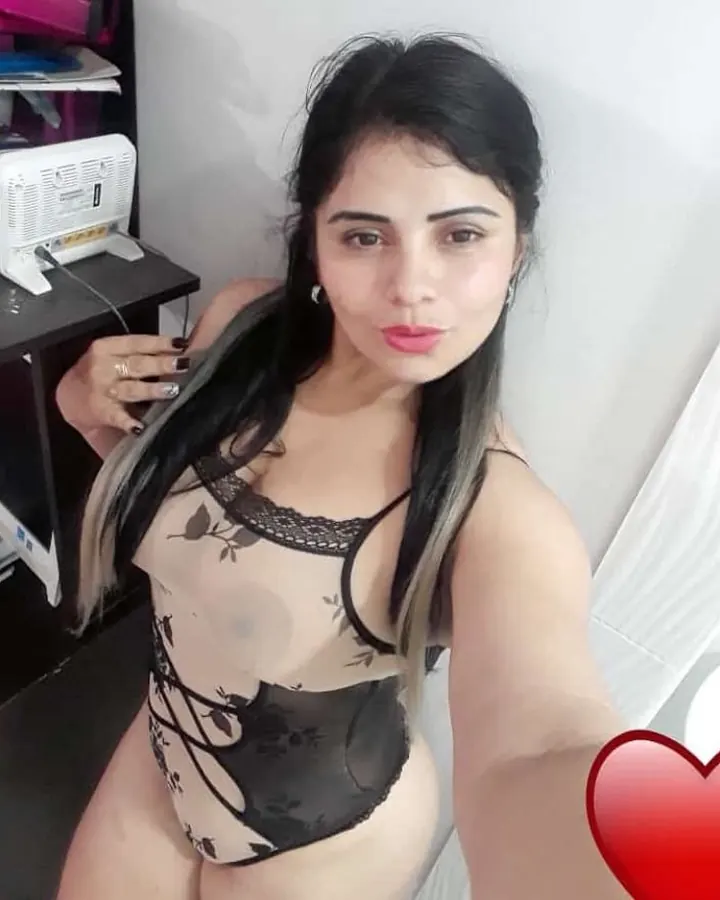 Femme aux cheveux noirs en body transparent noir avec dentelle, prenant un selfie devant un bureau.