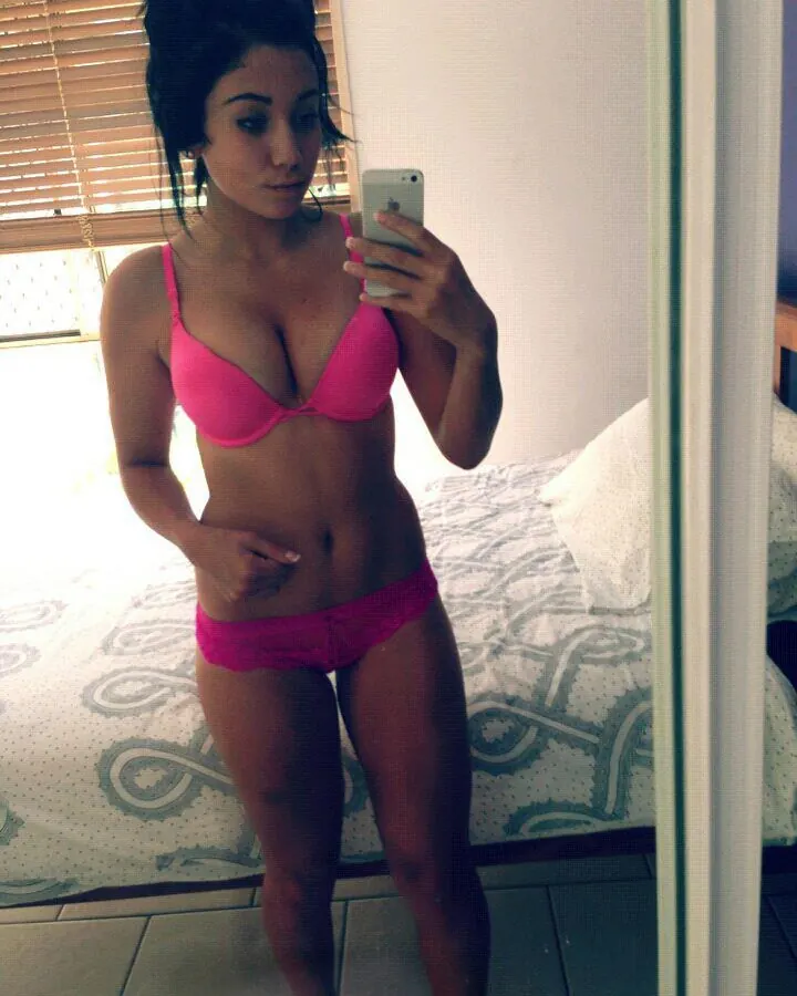 Femme aux cheveux noirs en lingerie noire, prenant un selfie dans un miroir, avec un tatouage visible sur le bras.