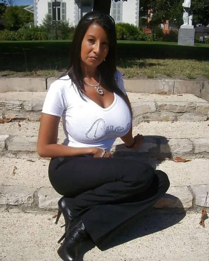 Femme aux cheveux noirs en bikini noir, posant sur une plage, les mains sur les hanches.