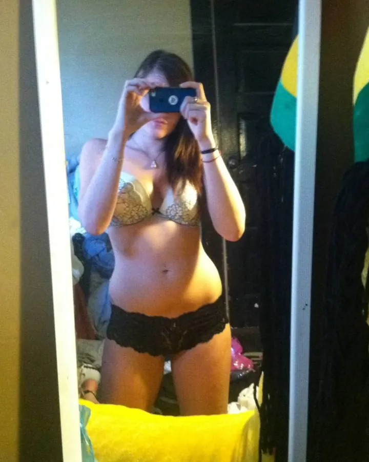 Femme en sous-vêtements noirs, prenant un selfie dans un miroir, pose détendue
