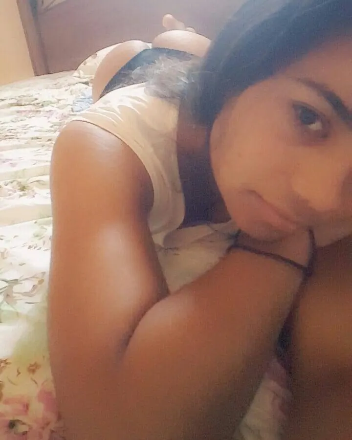Femme en haut blanc et bas jaune, prenant un selfie dans une salle de bain, tenant un téléphone rose
