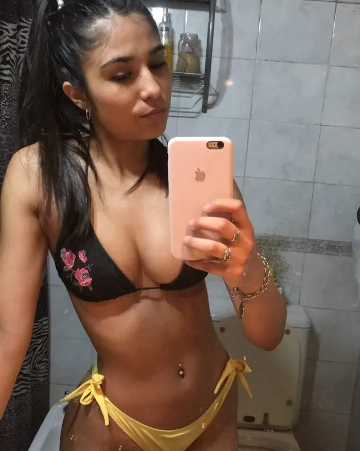 Femme en haut blanc et bas blanc, prenant un selfie, tenant un téléphone argenté, dans un cadre intérieur coloré