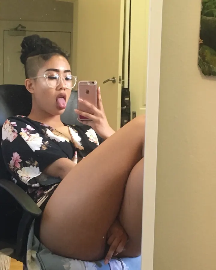 Femme arabe aux cheveux bruns, en sous-vêtements roses, prenant un selfie devant un miroir dans une salle de bain.