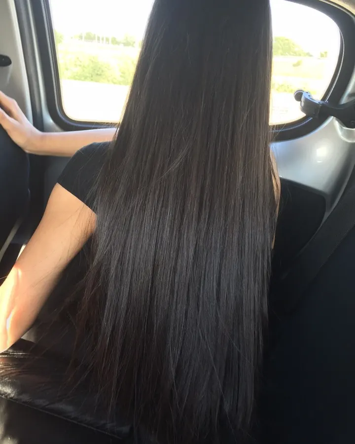 Dos d'une femme aux longs cheveux noirs, assise dans une voiture, regardant par la fenêtre.