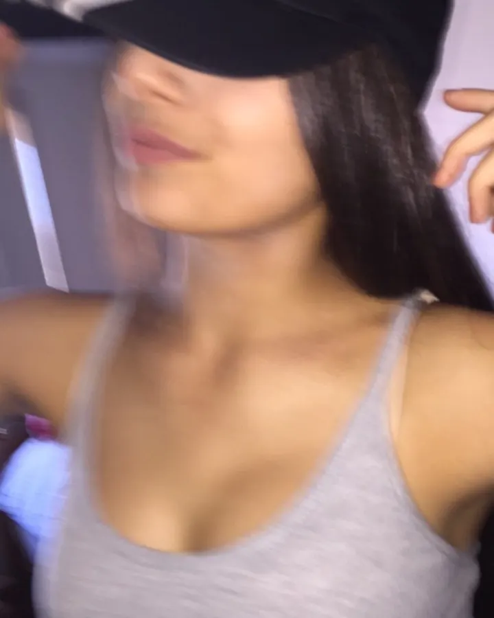 Femme aux cheveux noirs, en casquette Adidas, regardant de côté, en haut gris.