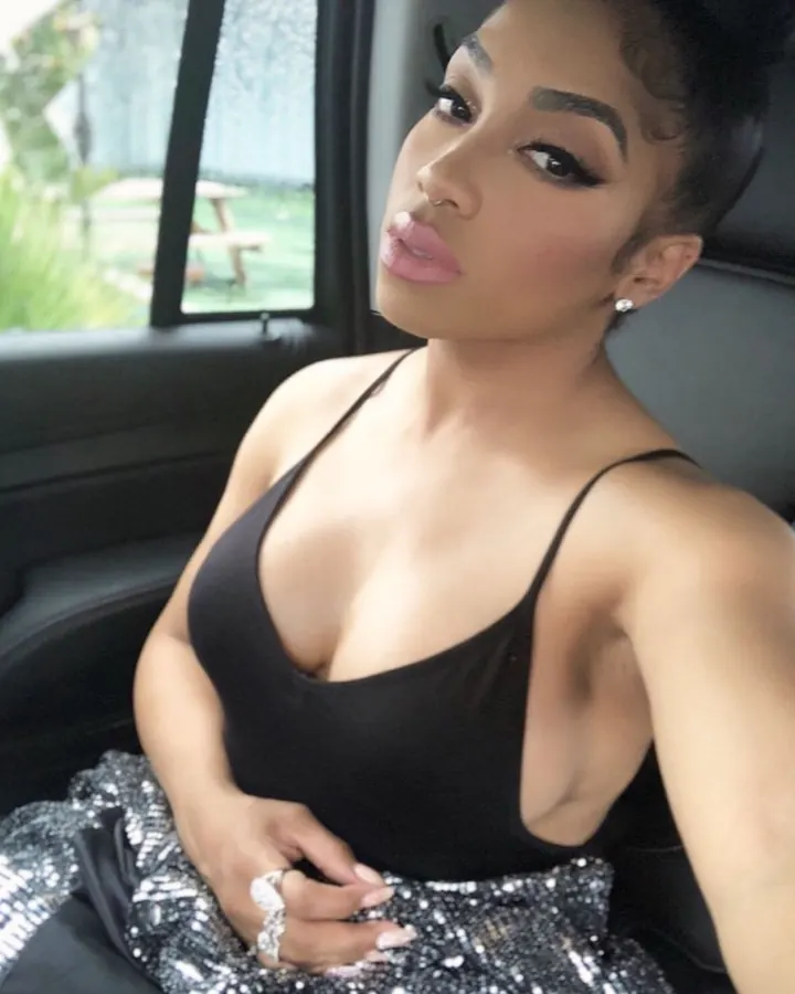 Femme assise dans une voiture, regardant vers l'appareil photo, portant un haut noir et une jupe pailletée.