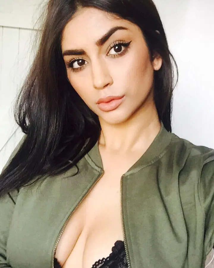 Jeune femme arabe en veste verte et soutien-gorge noir, prenant un selfie dans une pièce claire.